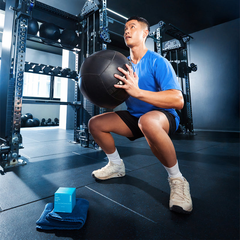 Man squatting with a medicine ball in a gym with Neuro Energy & Focus Mints pack on the floor