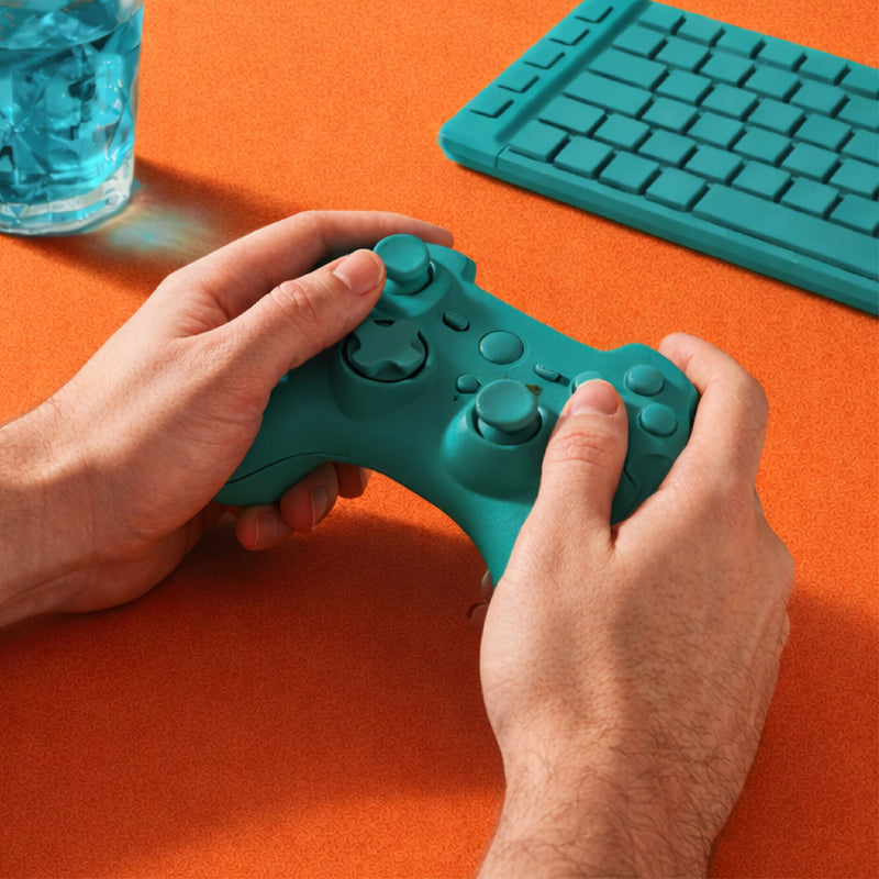 Person holding a gaming controller at a desk with keyboard and water glass